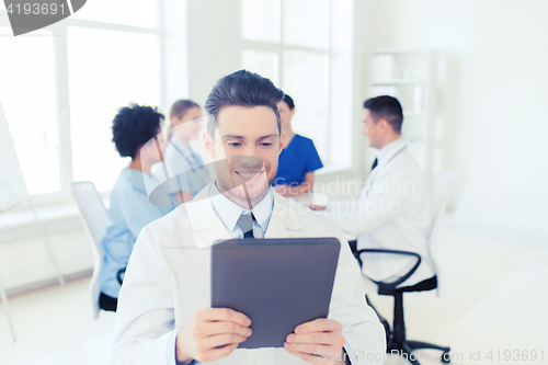 Image of happy doctor with tablet pc over team at clinic