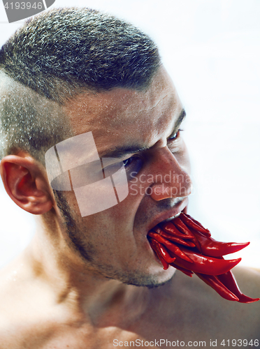 Image of desperate young man with a lot of chilli pepper in mouth, lookin