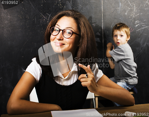 Image of little cute boy with young teacher in classroom studying at blackboard smiling, doing homework