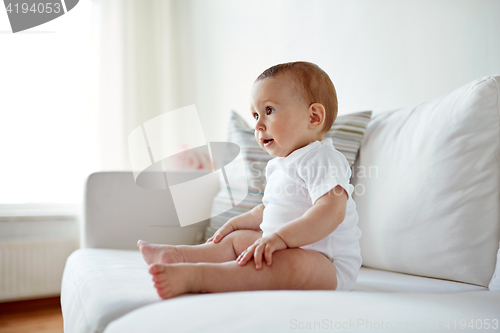 Image of happy baby boy or girl sitting on sofa at home