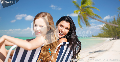 Image of happy women sunbathing in chairs on summer beach