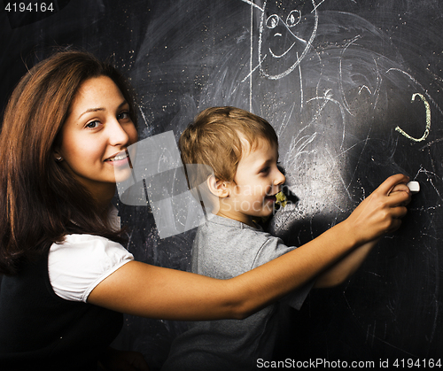 Image of little cute boy with young teacher in classroom studying at blackboard smiling, doing homework