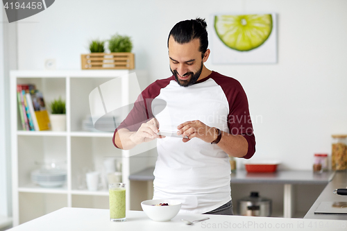 Image of man photographing breakfast by smartphone at home