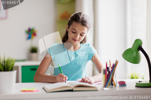Image of happy girl with book writing to notebook at home
