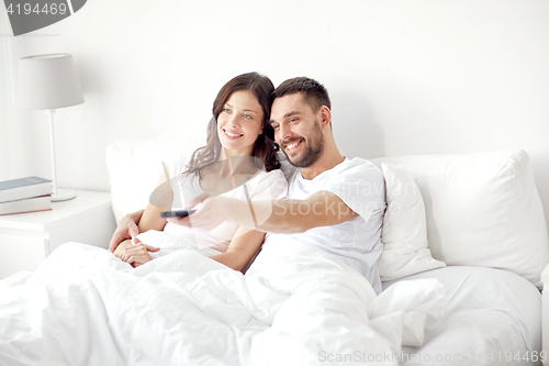 Image of happy couple lying in bed at home and watching tv