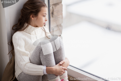 Image of sad girl sitting on sill at home window in winter