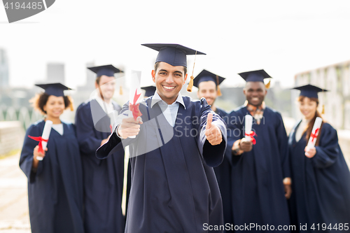 Image of happy students with diplomas showing thumbs up