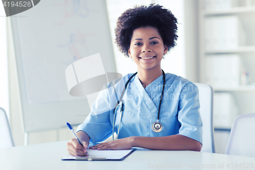 Image of happy female doctor or nurse writing to clipboard