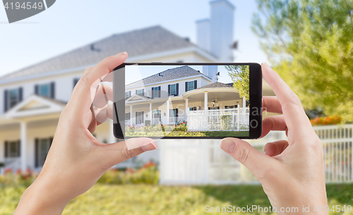 Image of Female Hands Holding Smart Phone Displaying Photo of House Behin