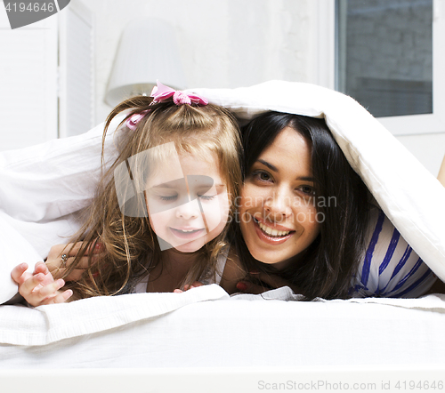 Image of mother with daughter together in bed smiling, happy family close up, lifestyle people concept, cool real modern family playing