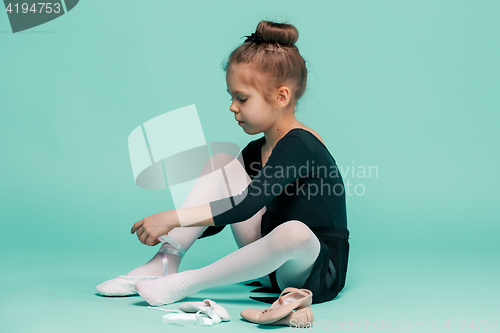 Image of Beautiful little ballerina in black dress for dancing puting on foot pointe shoes