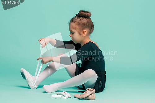 Image of Beautiful little ballerina in black dress for dancing puting on foot pointe shoes