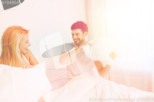 Image of happy couple having pillow fight in bed at home