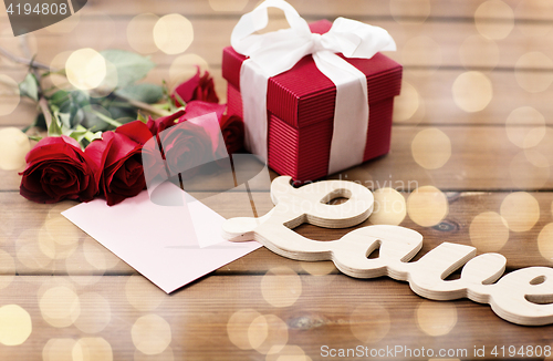 Image of close up of gift box, red roses and greeting card