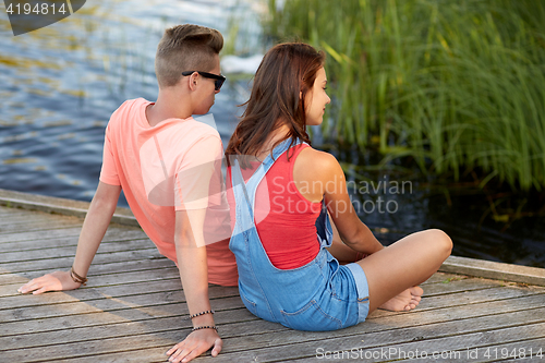 Image of happy teenage couple sitting on river berth