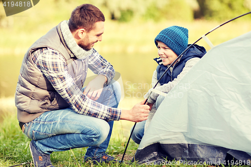 Image of happy father and son setting up tent outdoors