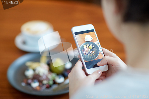 Image of woman with smartphone photographing food at cafe