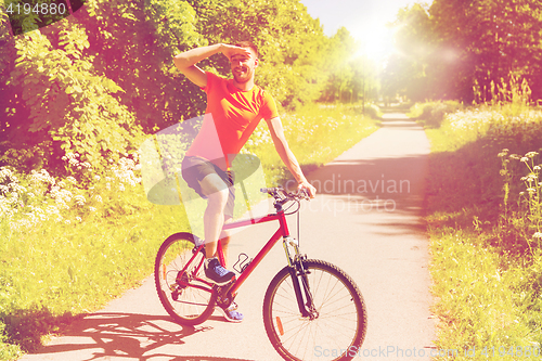 Image of happy young man riding bicycle outdoors