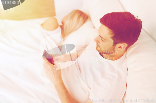 Image of man texting message while woman is sleeping in bed