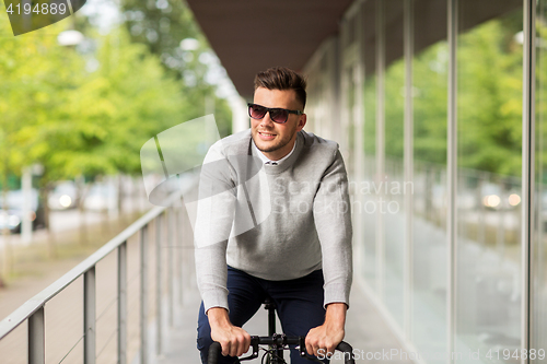 Image of young man in shades riding bicycle on city street