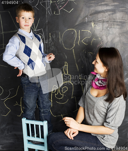 Image of little cute boy with young teacher in classroom studying at blackboard smiling, doing homework