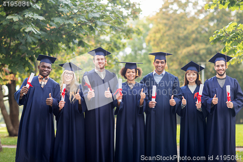 Image of happy students with diplomas showing thumbs up