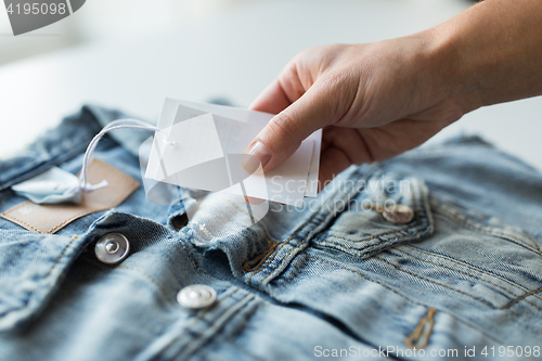 Image of close up of hand holding price tag of denim jacket