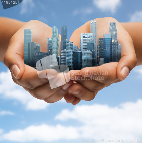 Image of hands holding city over blue sky background