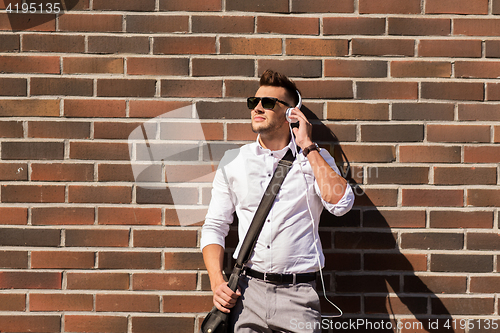 Image of young man in headphones with bag over brickwall