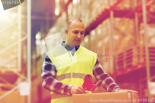 Image of man in safety vest packing box at warehouse