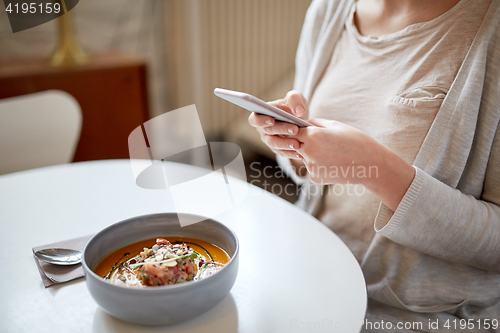 Image of woman with smartphone and pumpkin soup at cafe