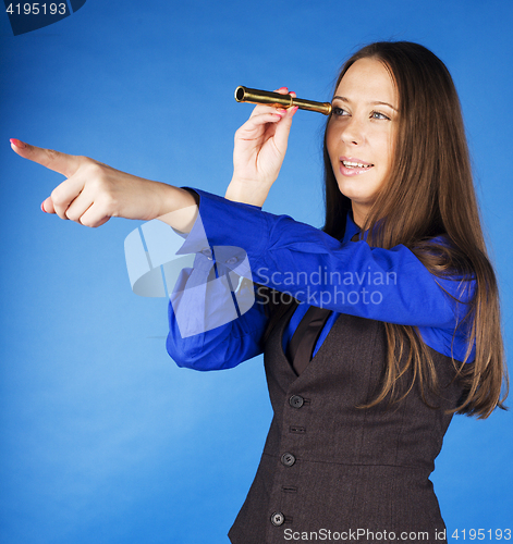 Image of young pretty brunette girl looking in spyglass and pointing on blue background, lifestyle travel people concept