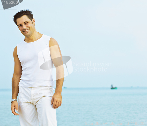 Image of young brunette man on beach at sea smiling, gomosexual in white 
