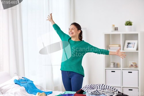 Image of happy woman packing travel bag at home