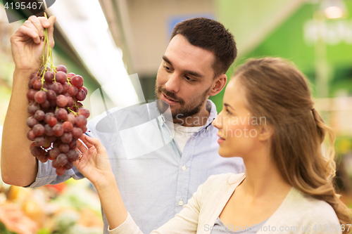 Image of happy couple buying grapes at grocery store