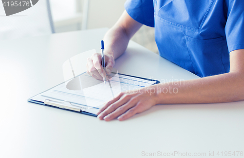 Image of close up of doctor or nurse writing to clipboard