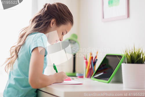 Image of girl with tablet pc writing to notebook at home