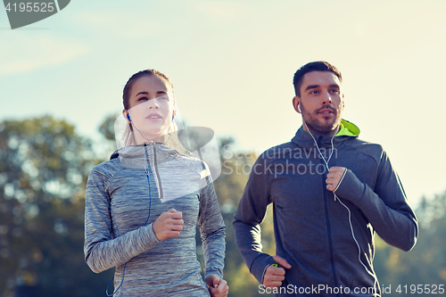 Image of happy couple with earphones running outdoors