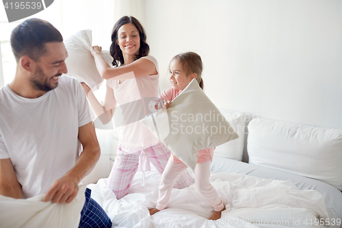 Image of happy family having pillow fight in bed at home