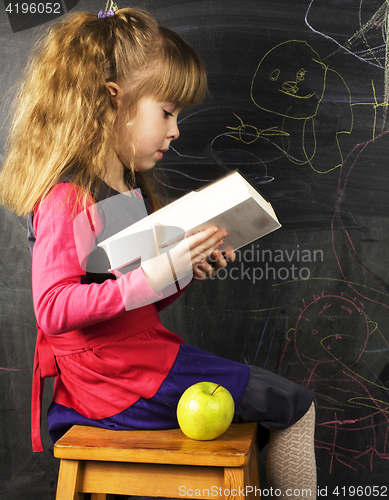 Image of portrait of cute little girl with book and green apple near blac
