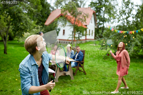 Image of happy friends playing badminton at summer garden