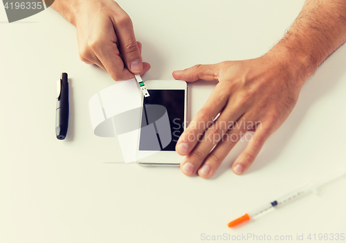 Image of close up of man with smartphone making blood test