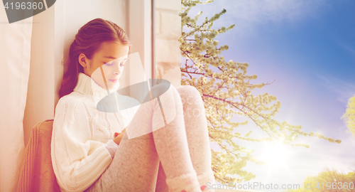 Image of sad girl sitting on sill at home window