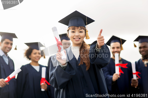 Image of happy students with diplomas showing thumbs up