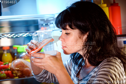 Image of Woman opened the refrigerator and sniffs a container of food