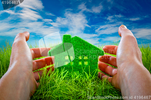 Image of Eco House in green grass protected by the human hands