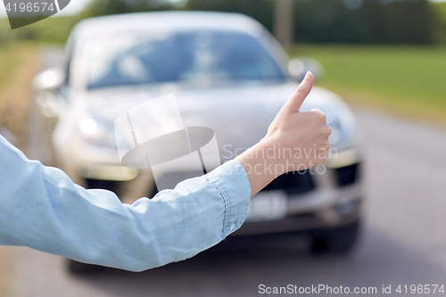 Image of woman hitchhiking and stopping car with thumbs up