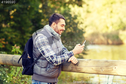 Image of happy man with backpack and smartphone outdoors