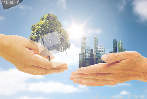 Image of hands holding green oak tree and city buildings