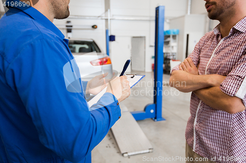 Image of auto mechanic with clipboard and man at car shop